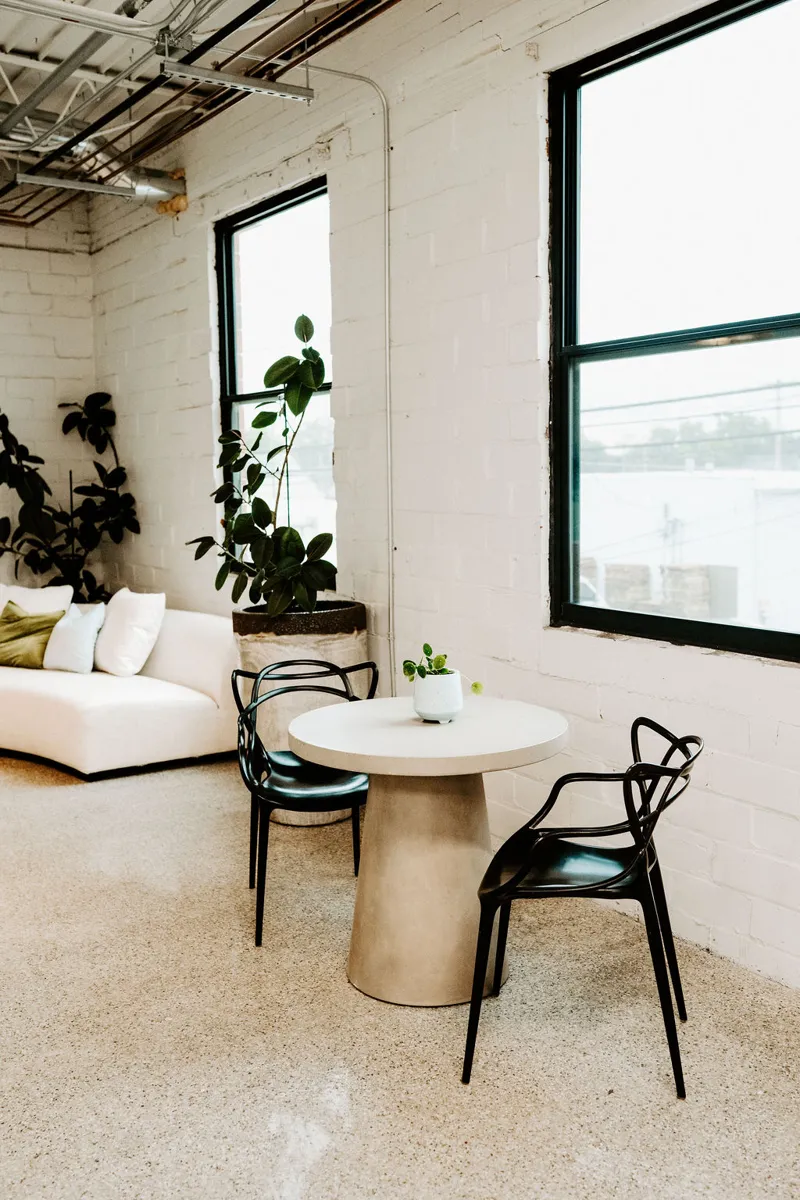 A small cafe table and chairs by the studio's tall windows